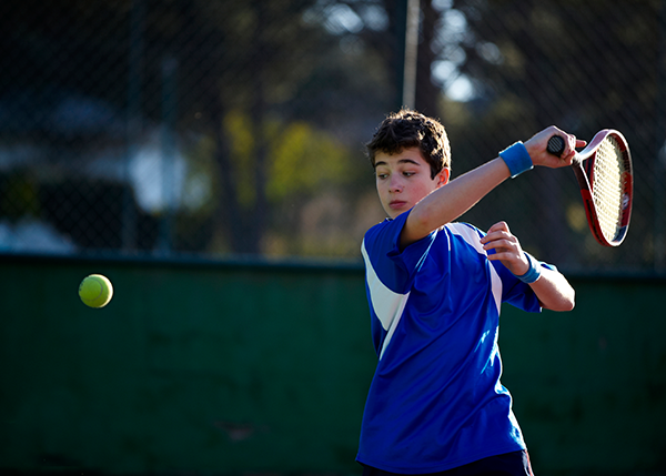 A junior teen tennis player smashes a forehand groundstroke back to his local tennis coach.