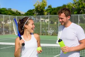 A man and woman laugh together after their adult group tennis lesson.