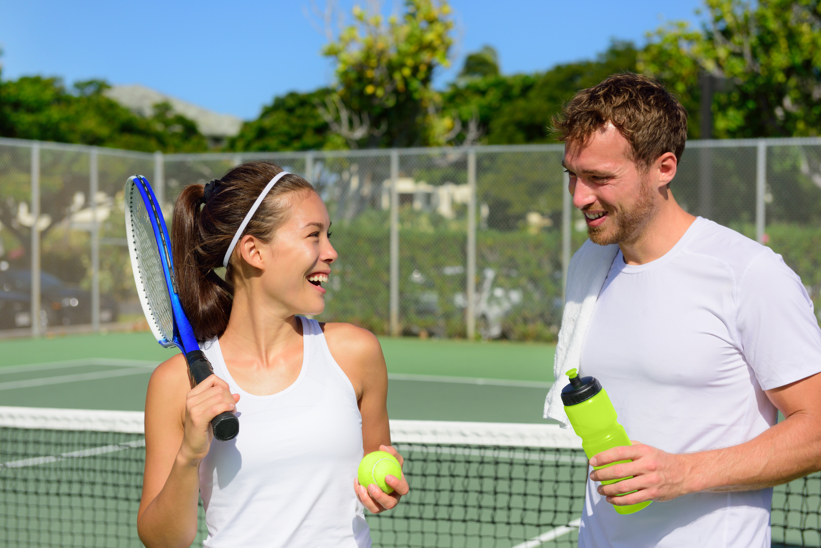 A man and woman laugh together after their adult group tennis lesson.